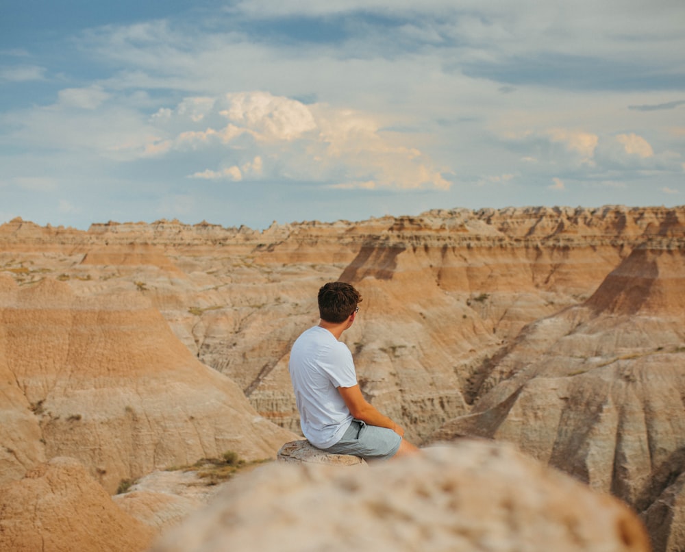 Hombre en camiseta blanca sentado en una formación rocosa marrón durante el día