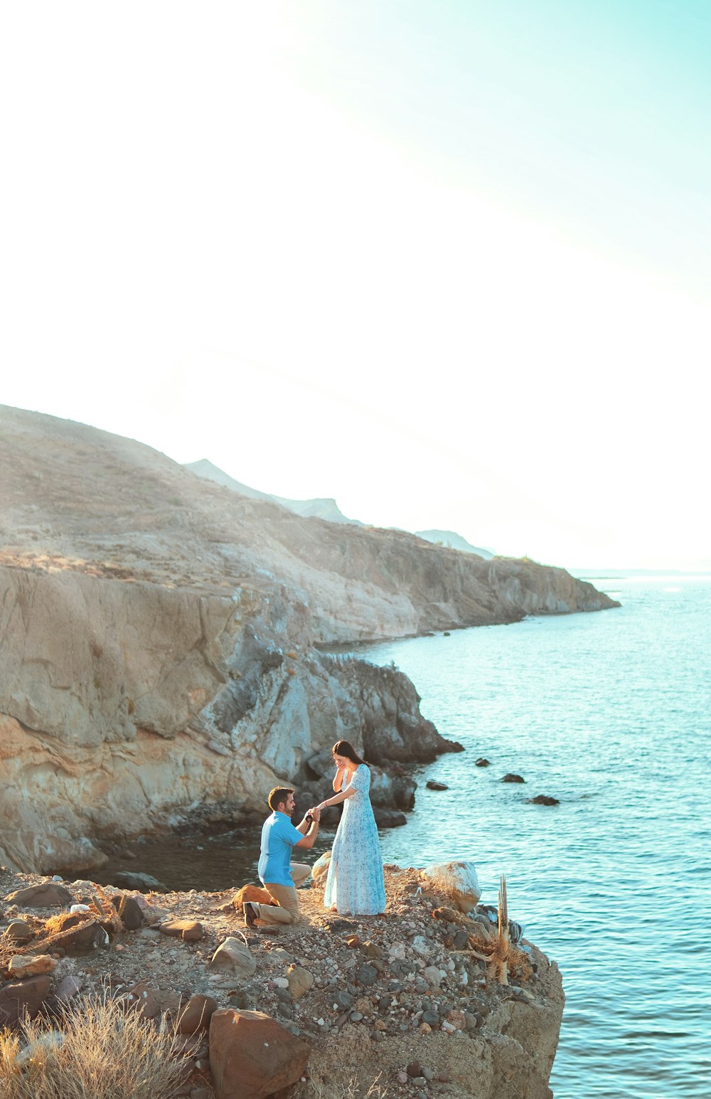 woman in blue denim jacket sitting on brown rock formation near body of water during daytime