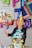 A child wearing a party hat is joyfully celebrating a birthday. They are holding a balloon themed with Super Mario characters. A colorful decorated cake with stars and various designs, including a '7' on it, is in front of the child. Background is adorned with balloons spelling out 'HAPPY' and numbers associated with birthday celebration.
