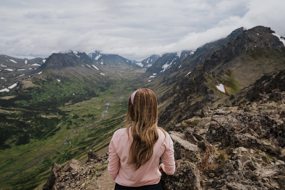 woman in pink long sleeve shirt sitting on rock mountain during daytime