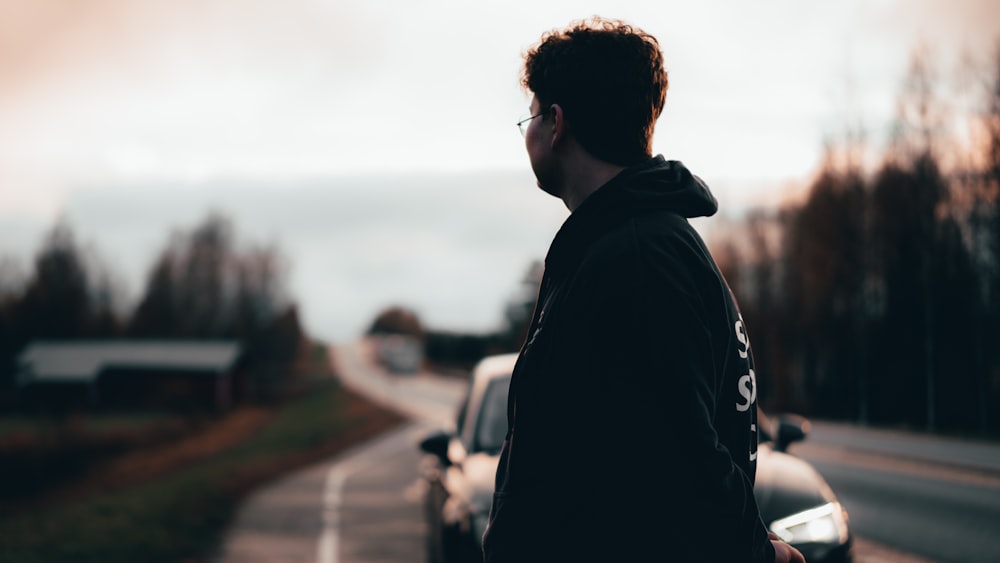man in black hoodie standing on road during daytime