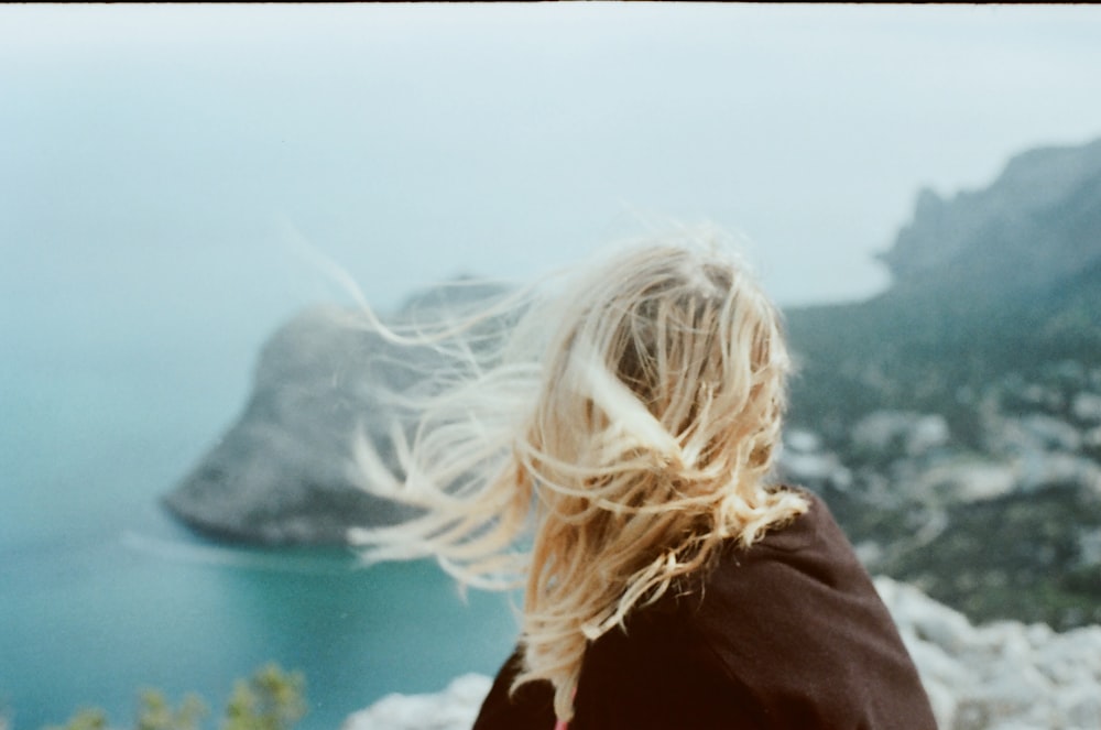 woman in black coat standing near body of water during daytime