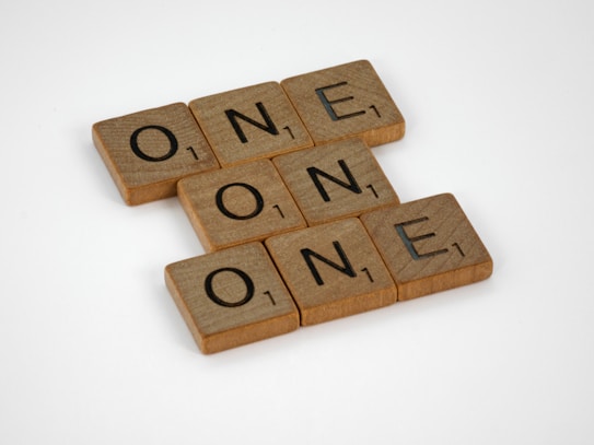 Wooden Scrabble tiles arranged to spell the word 'ONE' in a crossword-like fashion on a plain white background.