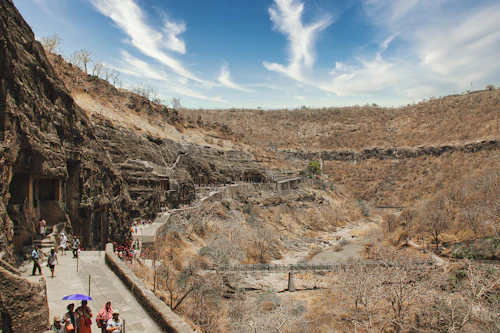 Visitors walking a stone path below a rocky brown hill near Aurangabad