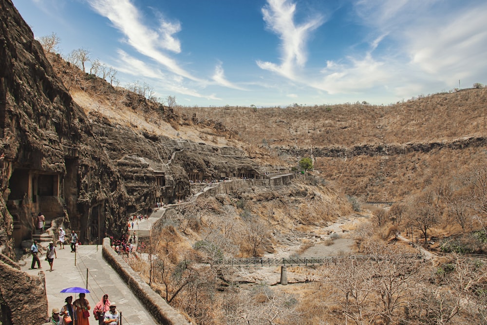 people walking on pathway near brown mountain under blue sky during daytime