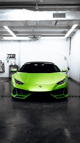Close-up of a sleek car engine with green accents under bright garage lights.
