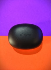 A black, oval-shaped case with the brand name 'realme' printed on it sits against a vibrant background divided into a purple upper half and an orange lower half. The sleek, matte finish of the case creates a modern and sophisticated appearance.