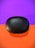A black, oval-shaped case with the brand name 'realme' printed on it sits against a vibrant background divided into a purple upper half and an orange lower half. The sleek, matte finish of the case creates a modern and sophisticated appearance.