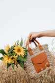 A smiling woman holding a medium-sized crochet tote bag in a sunny garden.