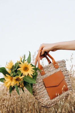 A smiling woman holding a medium-sized crochet tote bag in a sunny garden.