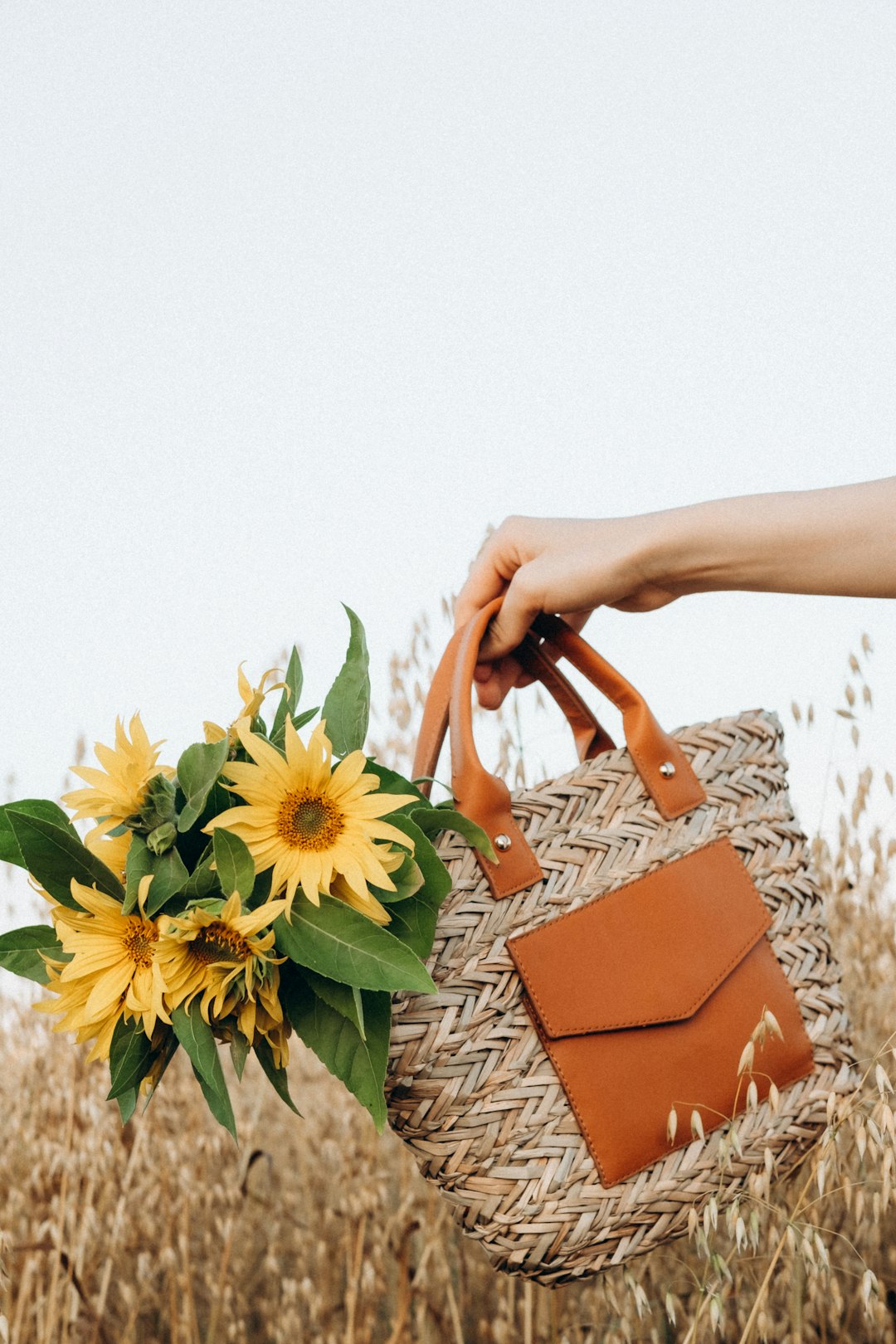 person holding brown leather handbag with yellow sunflower