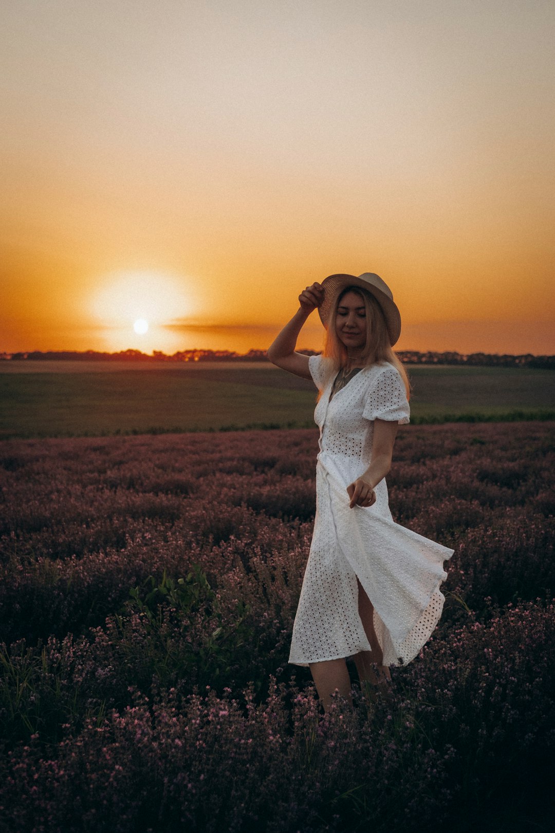woman in white dress standing on green grass field during sunset