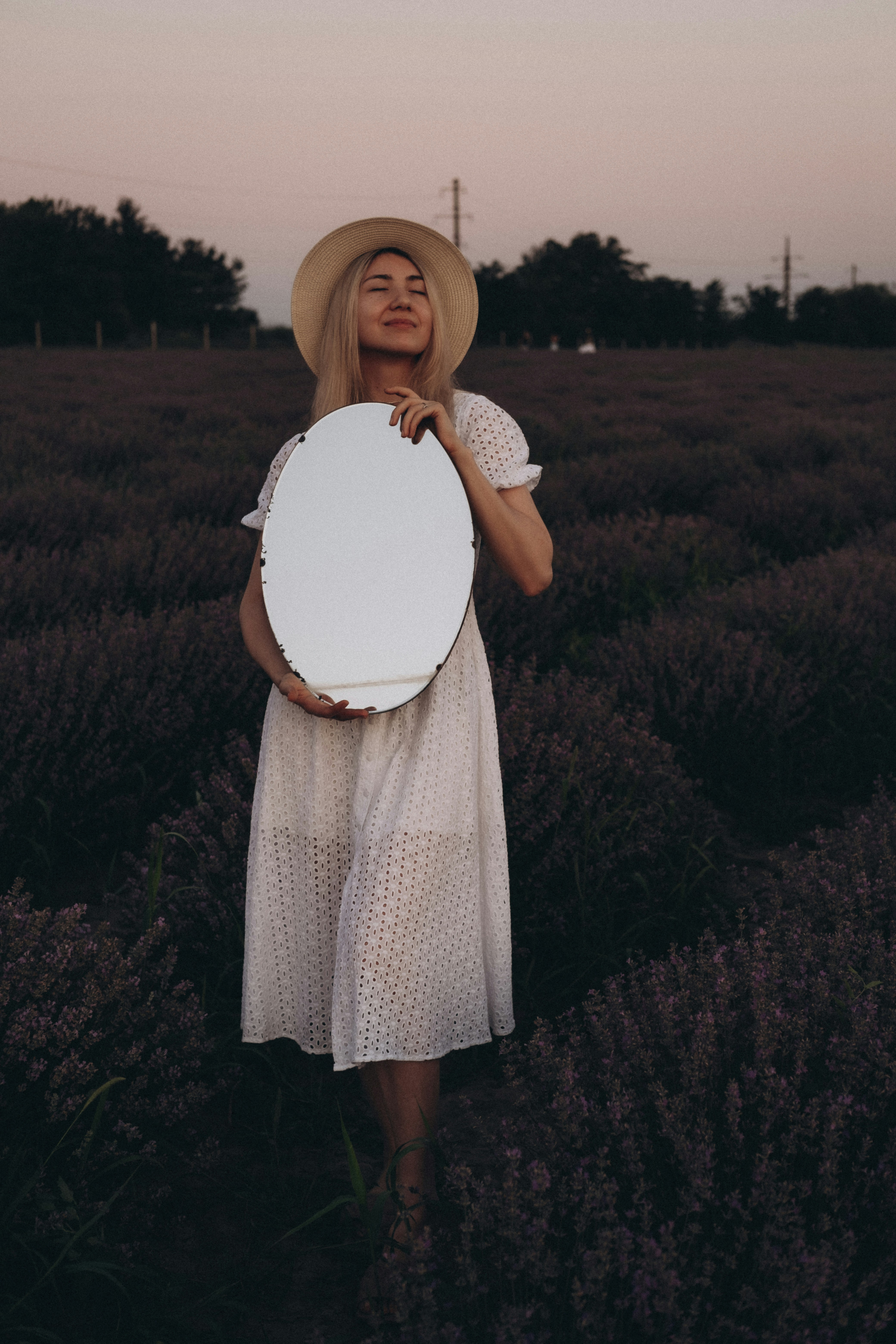 woman in white dress holding white hat standing on green grass field during daytime