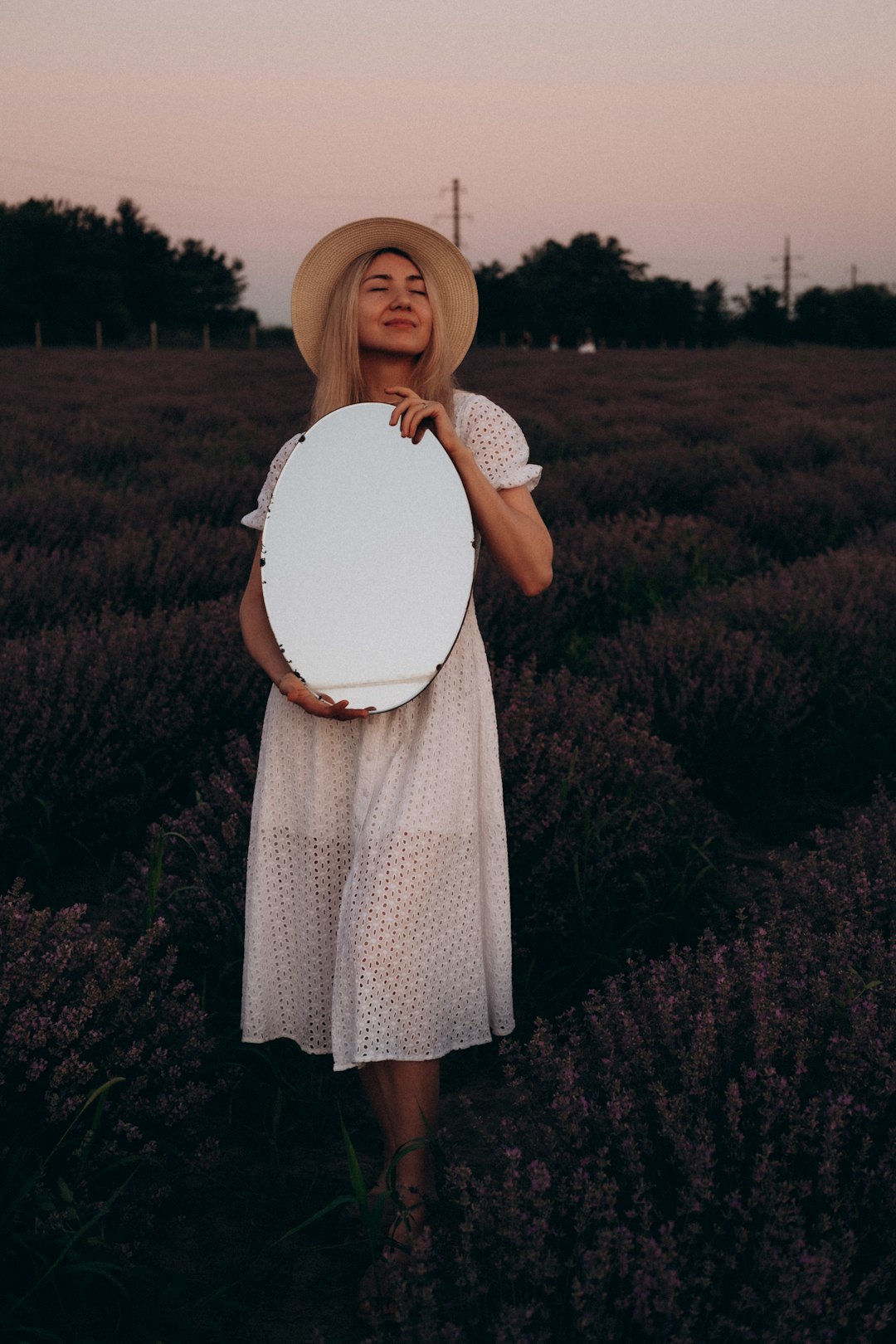 woman in white dress holding white hat standing on green grass field during daytime