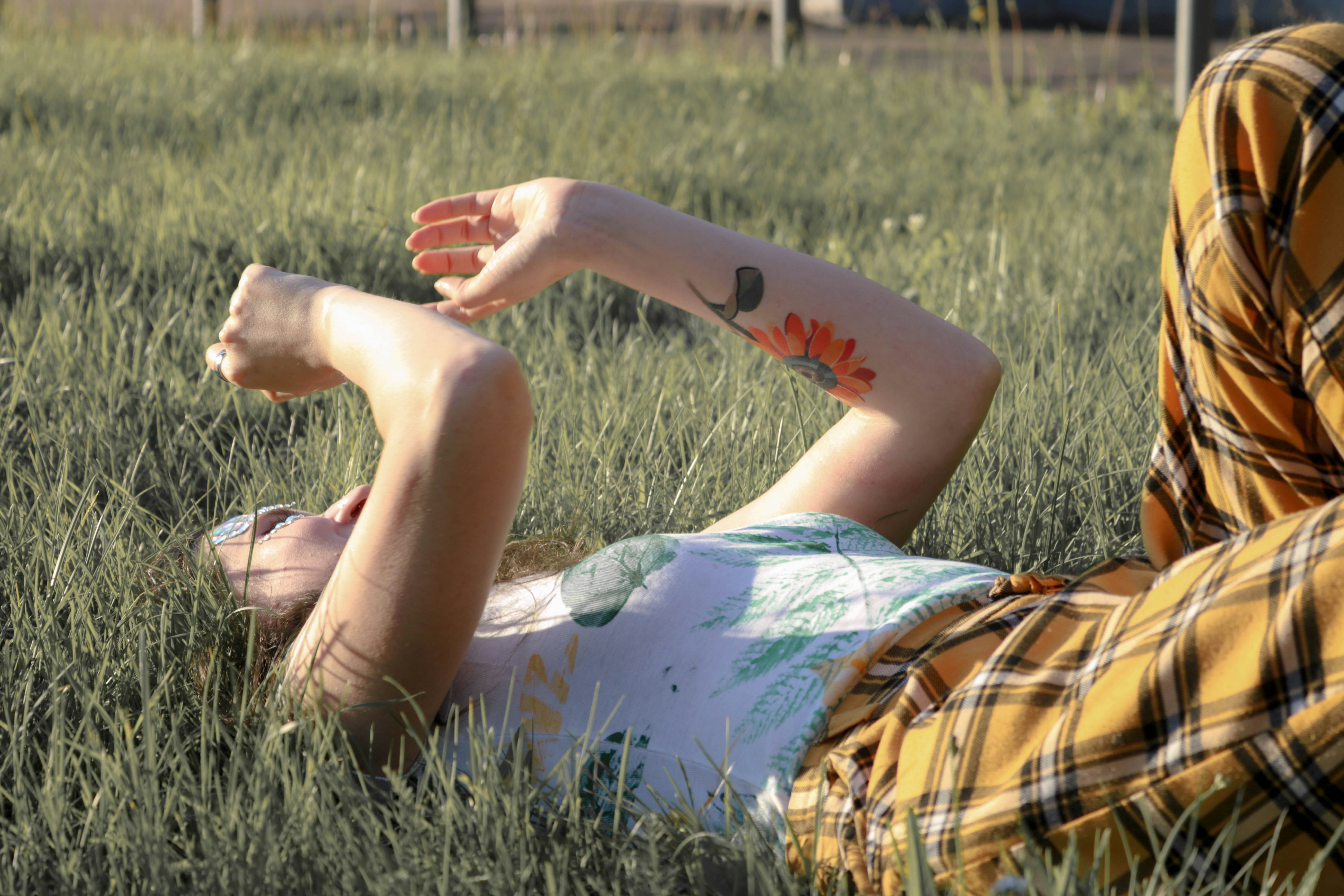 woman in white and brown floral dress lying on green grass field during daytime