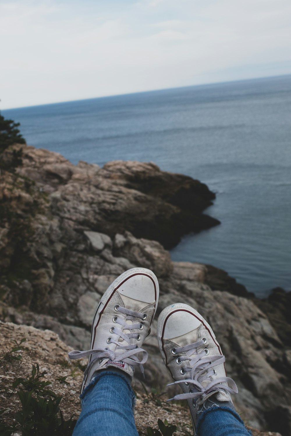 person wearing gray and white sneakers standing on brown rock formation near body of water during