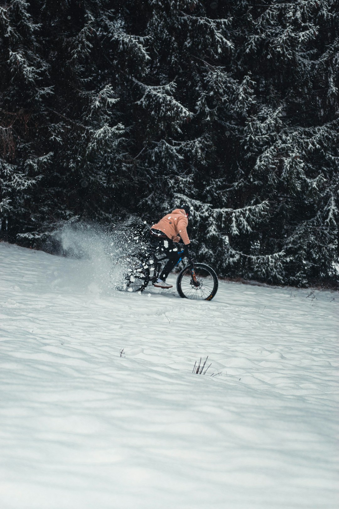 person in orange jacket riding bicycle on snow covered ground during daytime