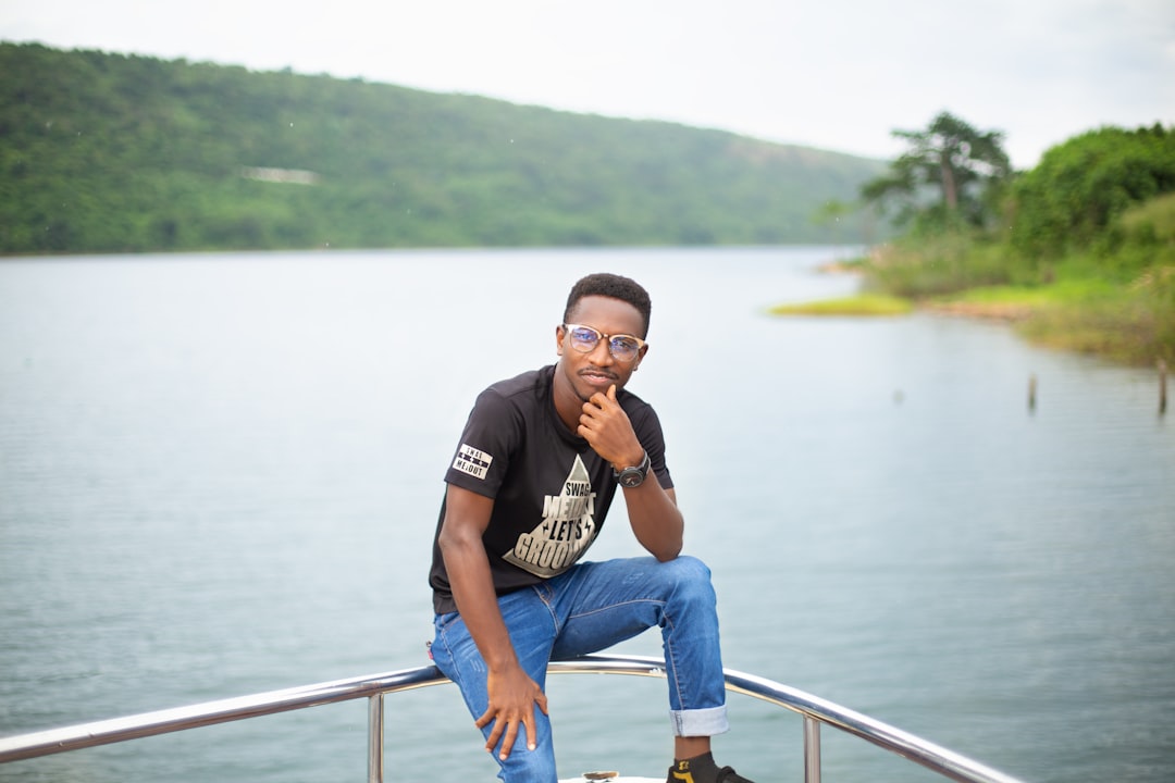 man in black crew neck t-shirt and blue denim jeans sitting on stainless steel railings