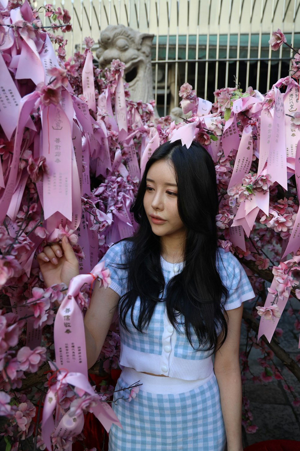 woman in white and blue plaid shirt standing beside pink flowers