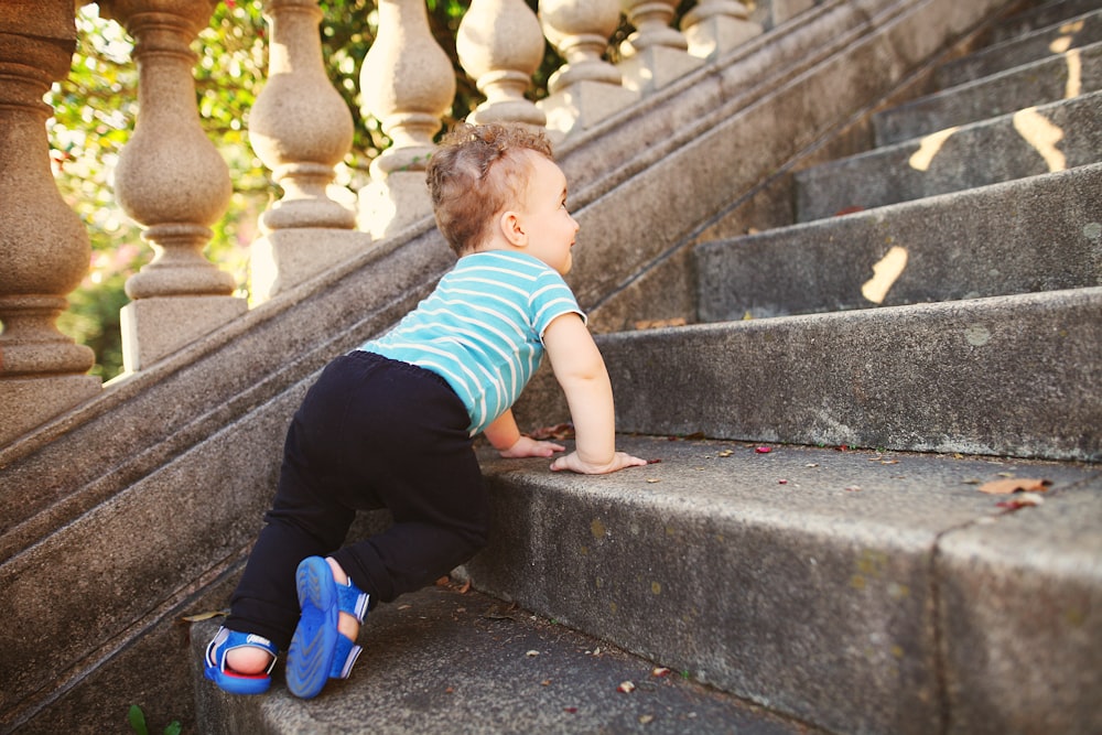 boy in green and white striped t-shirt and black pants sitting on concrete stairs during