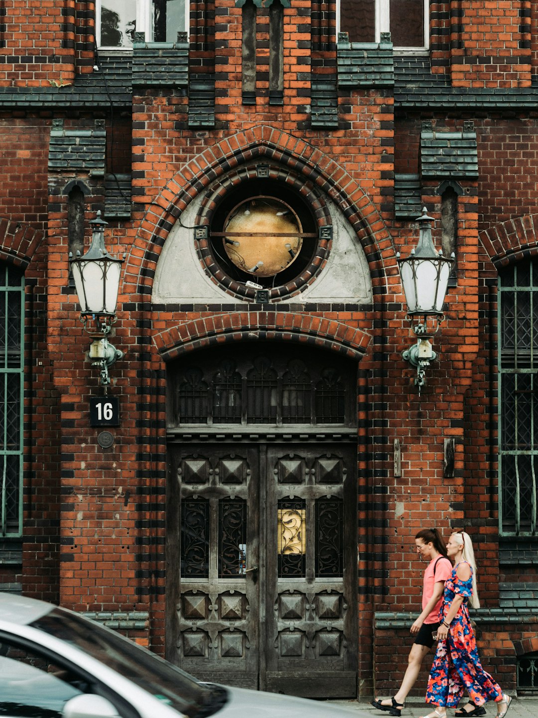 woman in red jacket standing in front of brown brick building