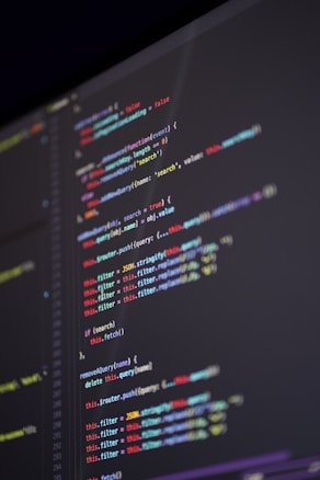 A close-up view of computer code displayed on a dark screen, featuring syntax highlighted in various colors such as red, blue, green, and yellow against a black background. The code appears to be JavaScript, containing functions, variables, and commands.