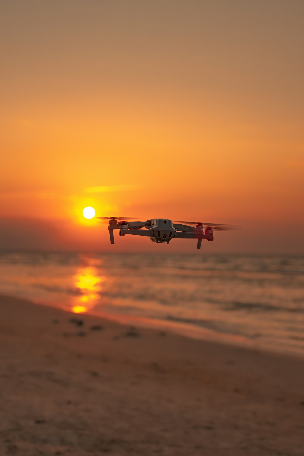 white drone flying over the beach during sunset