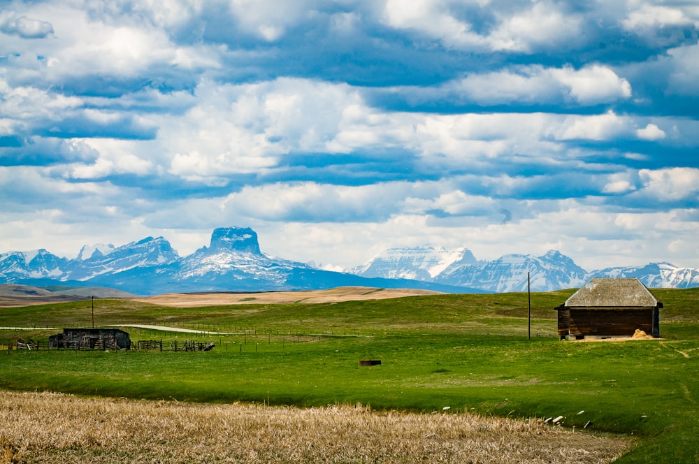 green grass field near mountain under white clouds during daytime