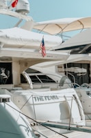 Several luxurious yachts are docked in a marina. One of the yachts prominently features an American flag and has the name 'The Pearl' written on it. The yachts are equipped with various amenities and have a sleek, modern design.
