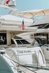 Several luxurious yachts are docked in a marina. One of the yachts prominently features an American flag and has the name 'The Pearl' written on it. The yachts are equipped with various amenities and have a sleek, modern design.