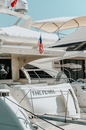 Several luxurious yachts are docked in a marina. One of the yachts prominently features an American flag and has the name 'The Pearl' written on it. The yachts are equipped with various amenities and have a sleek, modern design.