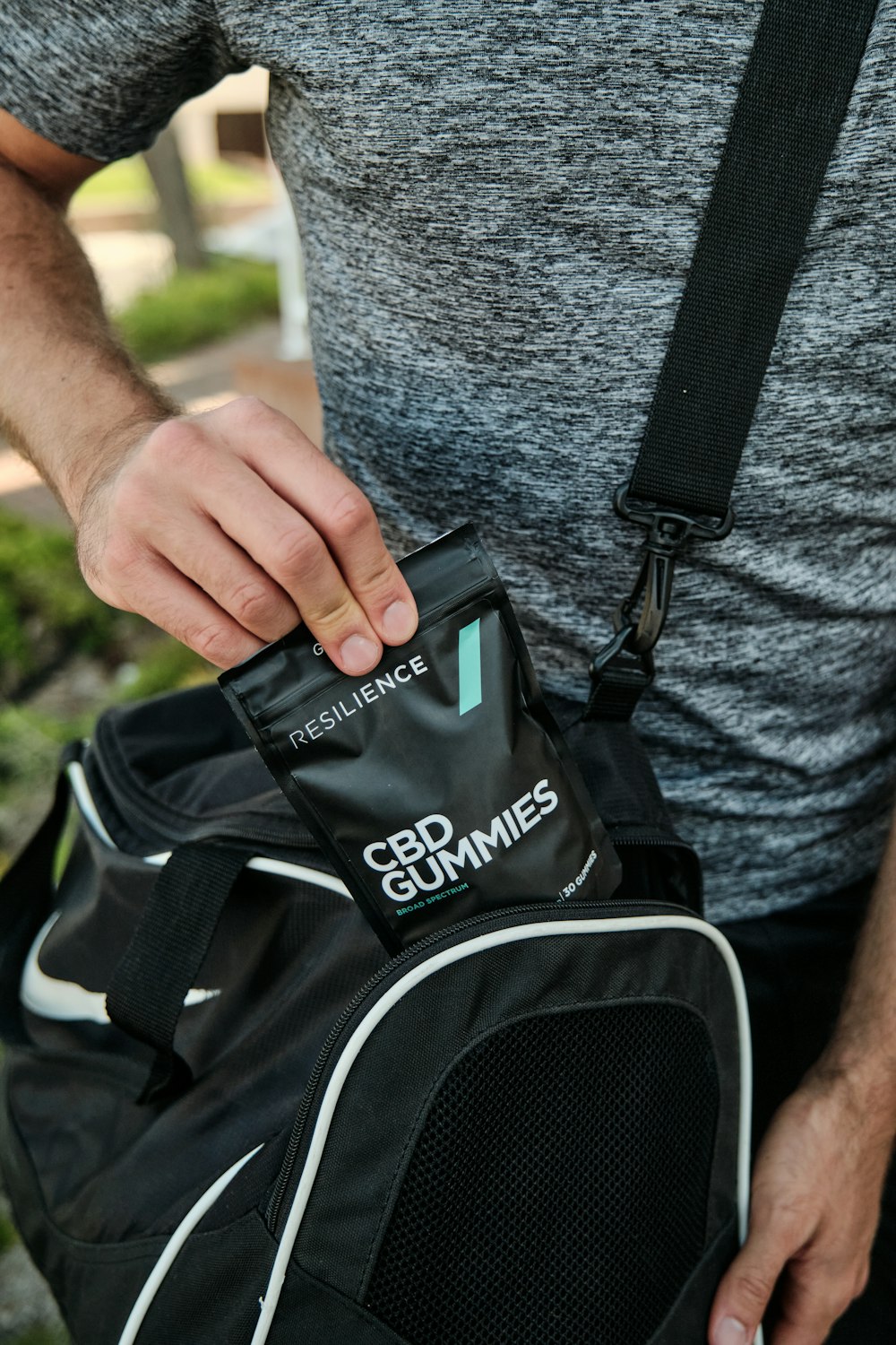 person in gray shirt holding black adidas backpack