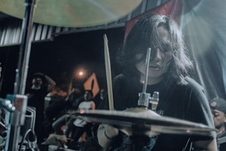 Shaan Frenƶy passionately playing drums on a dimly lit stage with metal band energy.