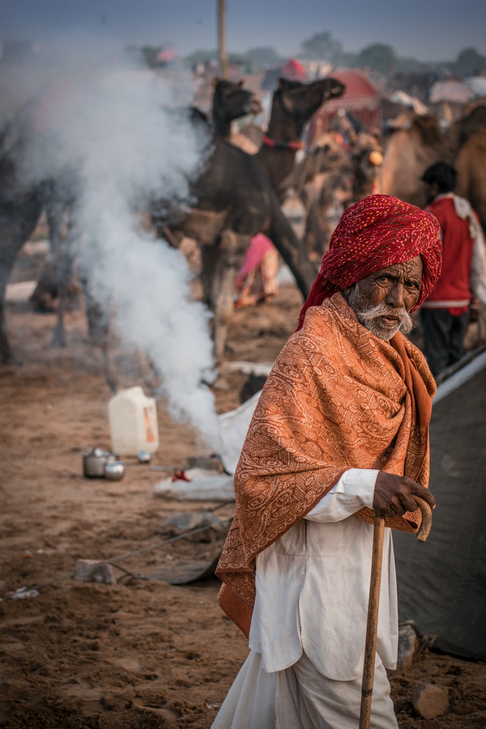 man in red turban and brown robe sitting on ground