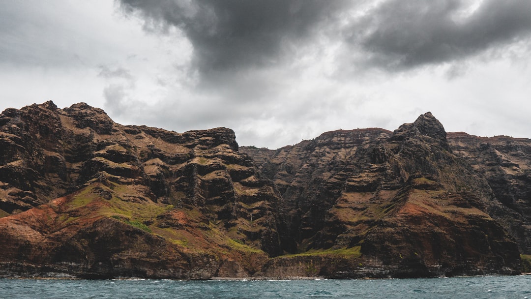 brown rocky mountain beside body of water under cloudy sky during daytime