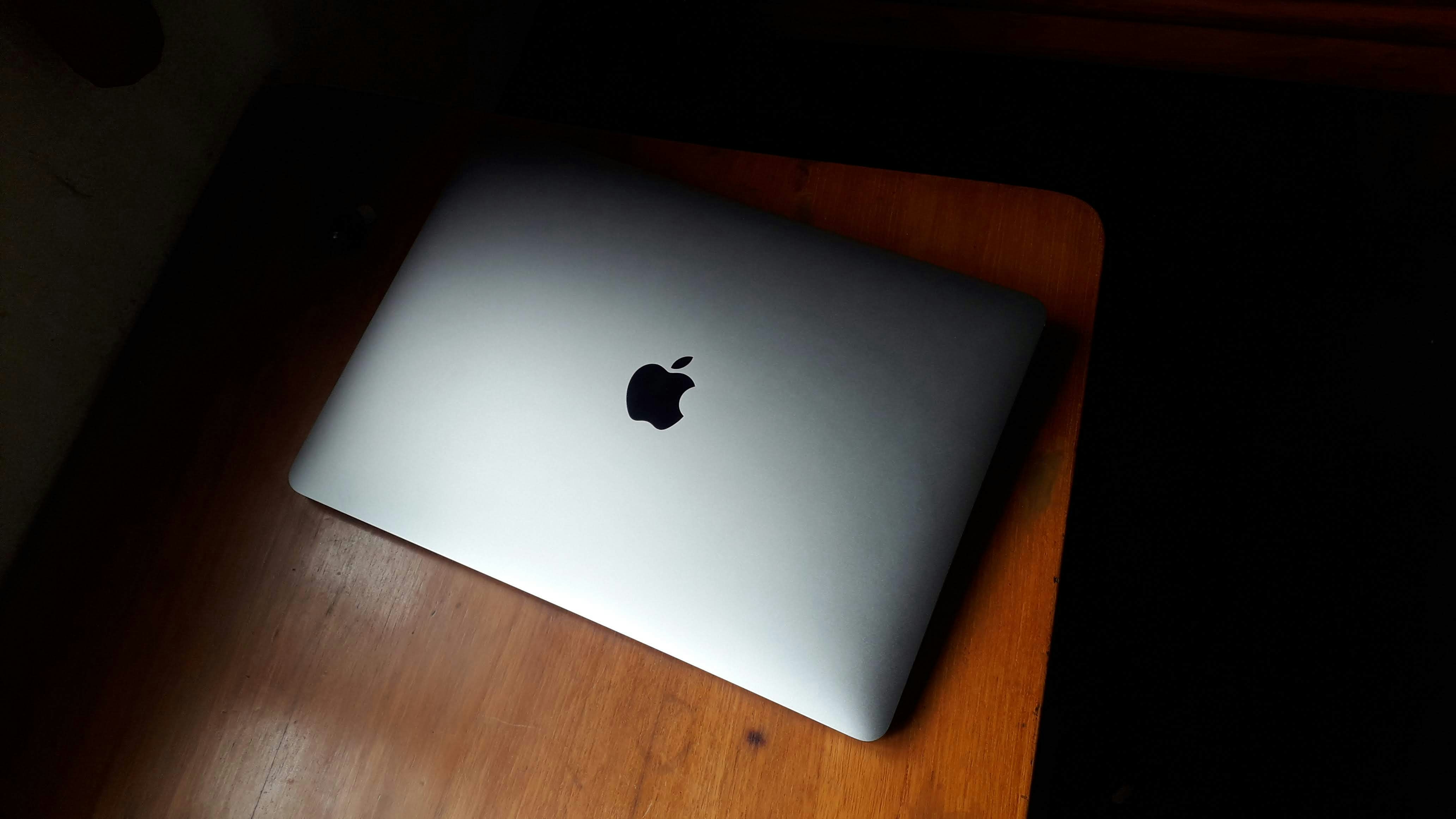MacBook Pro open on minimal dark desk with ambient low-key lighting and atmospheric shadows