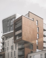 A modern multi-story residential building with a combination of materials, including glass, metal, and brown paneling. The architecture features a mix of rectangular shapes with several protruding balconies, providing contrast between smooth white and textured brown surfaces. Large windows dominate the upper floors, allowing for natural light to enter.