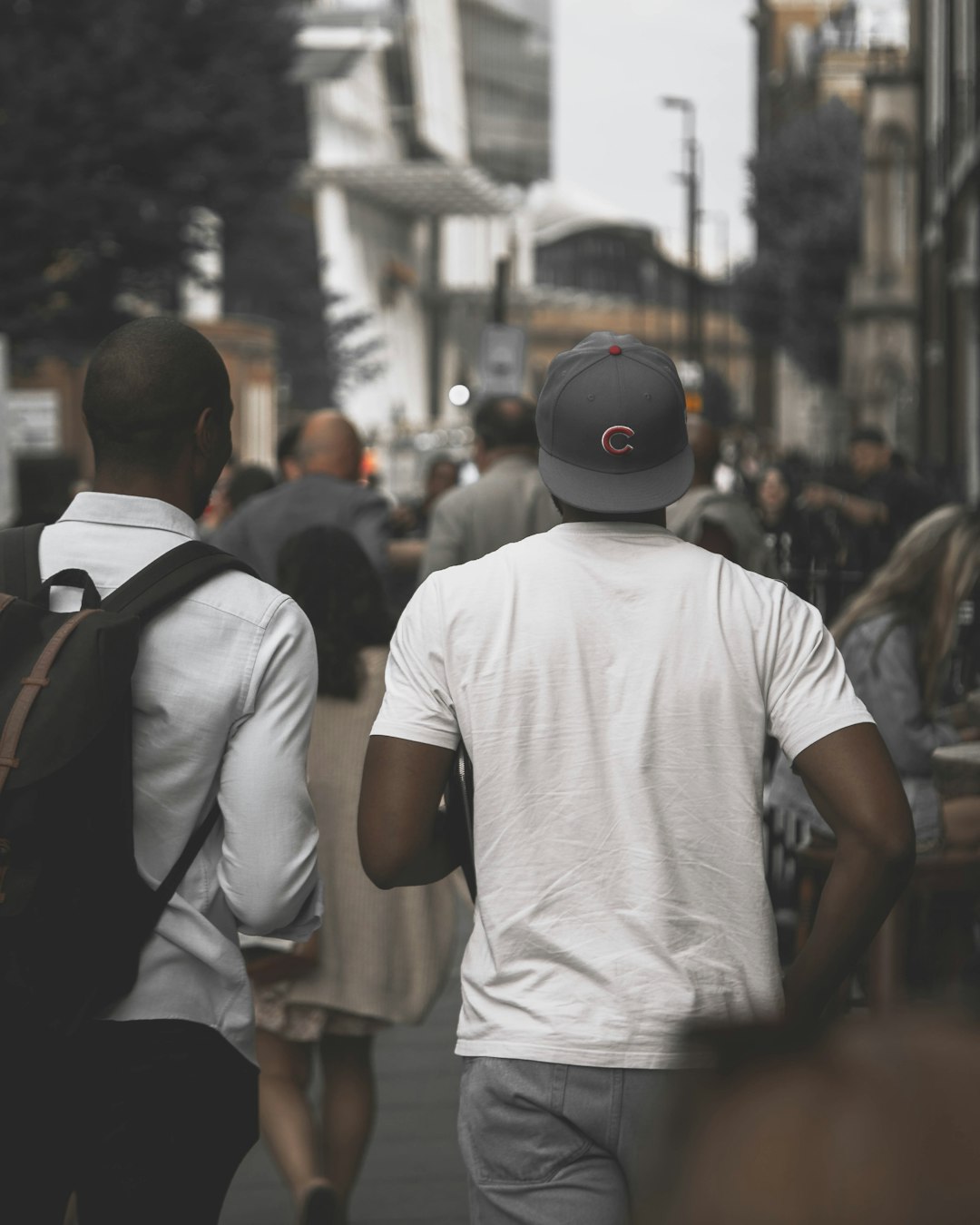 man in white crew neck t-shirt wearing black backpack walking on street during daytime
