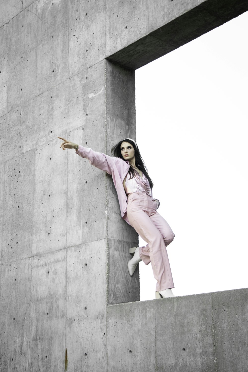 회색 콘크리트 벽에 서 있는 분홍색 코트를 입은 여자