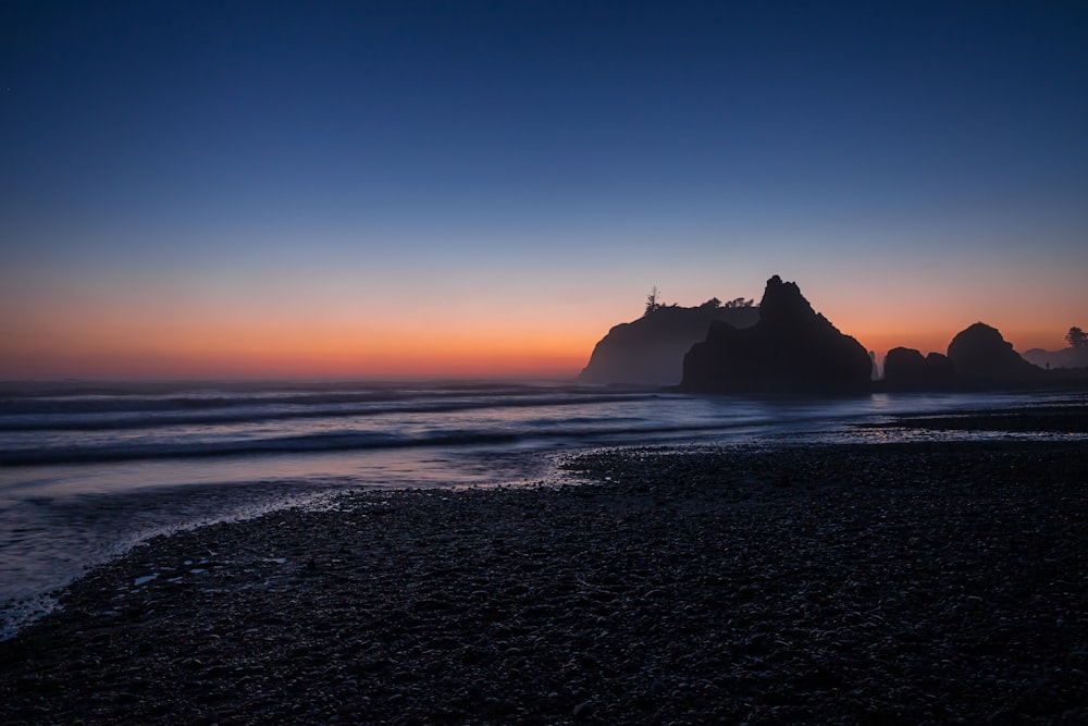 silhueta da formação rochosa no mar durante o pôr do sol
