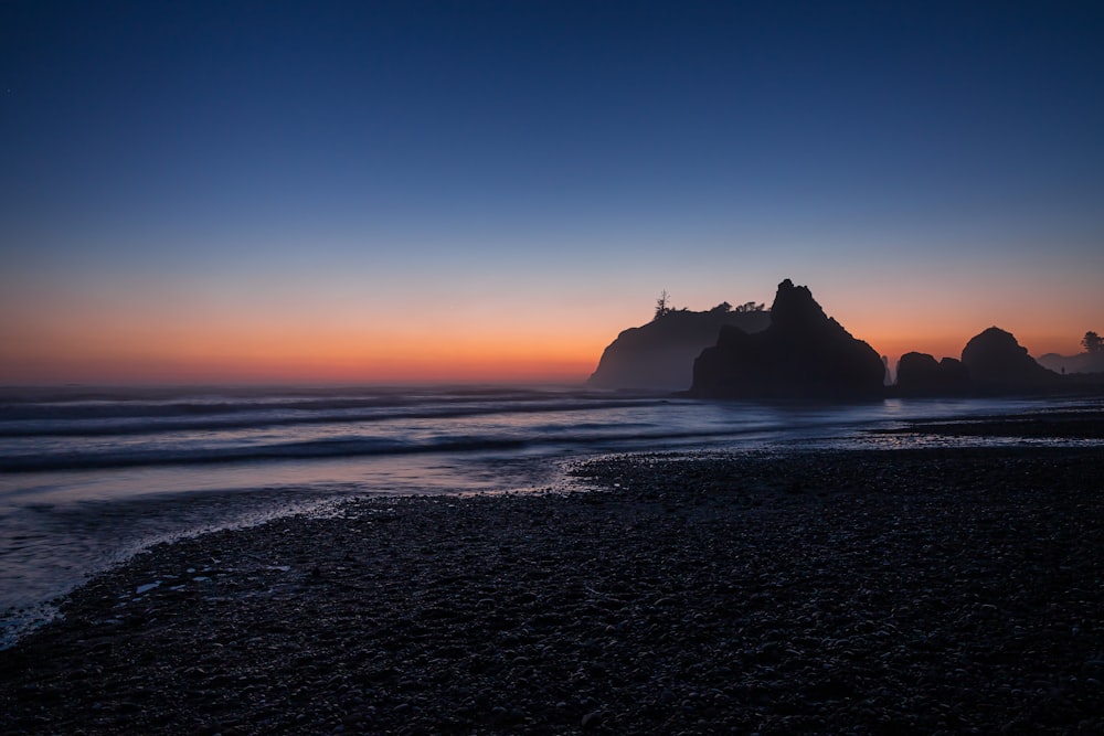 silhouette of rock formation on sea during sunset