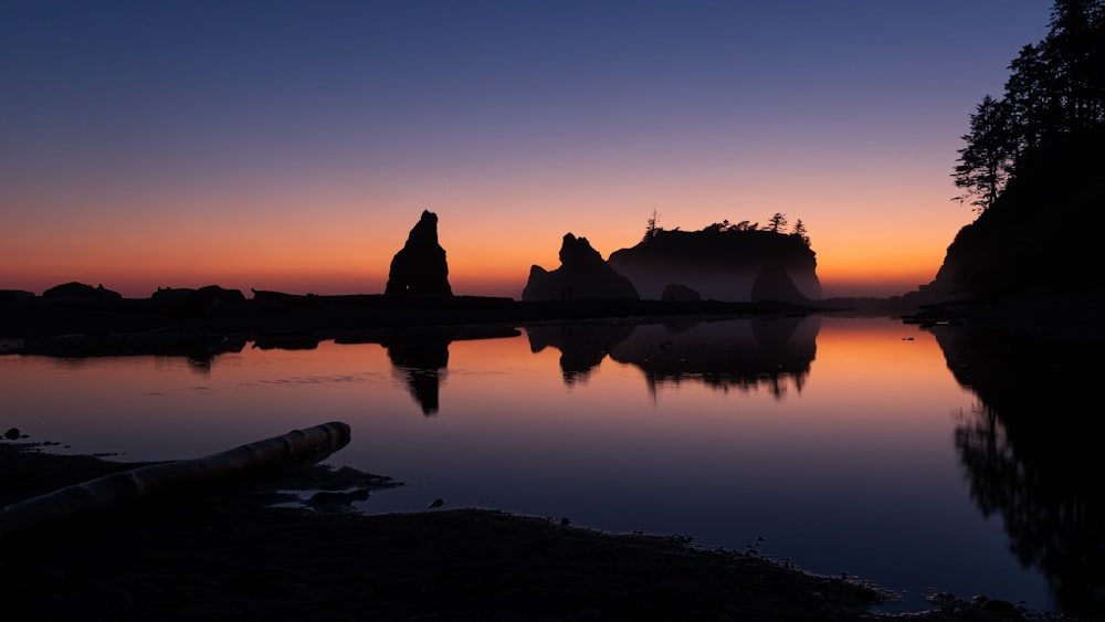 夕暮れ時の水辺の岩の上に座っている2人のシルエット