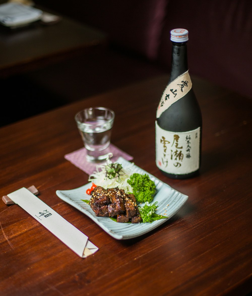 white and black labeled bottle beside clear drinking glass on brown wooden table