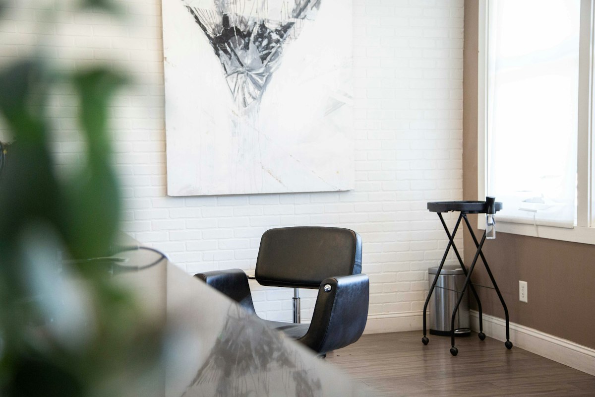 A black salon chair beside a white brick wall with a large abstract painting
