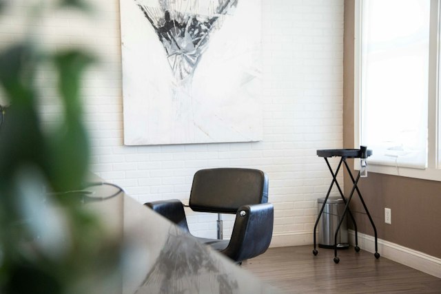 A black salon chair beside a white brick wall with a large abstract painting