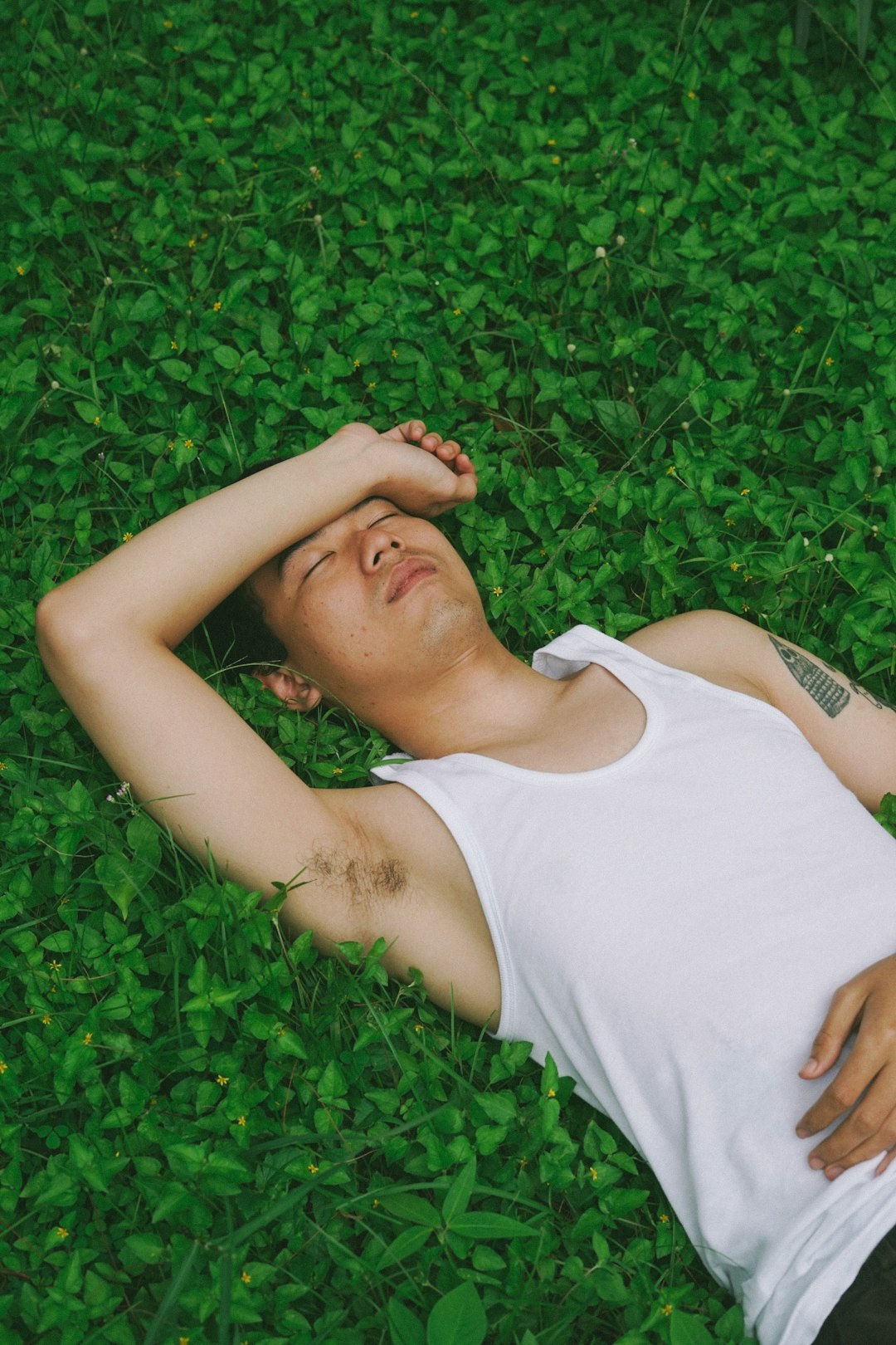 woman in white tank top lying on green grass