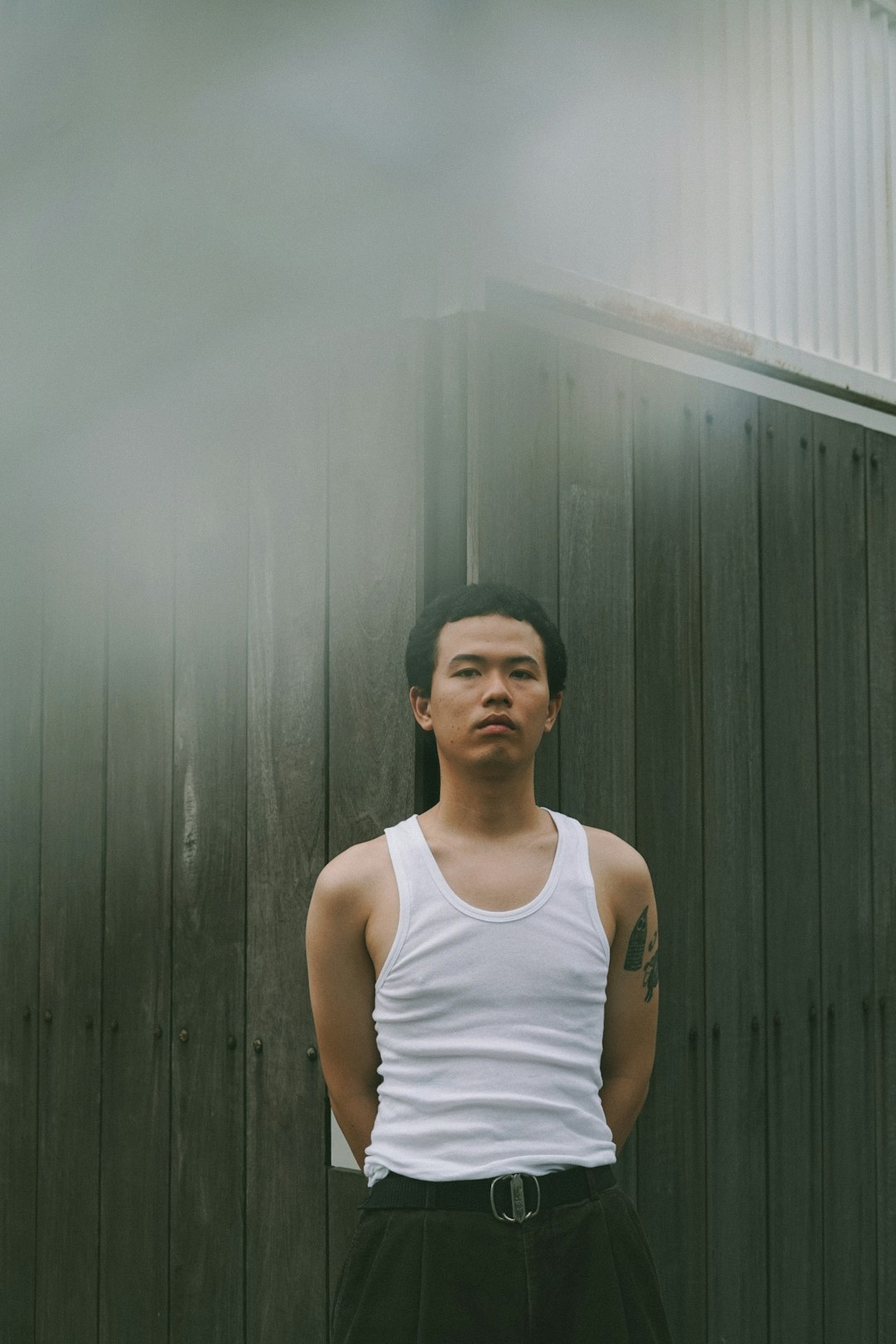 man in white tank top standing near gray wall