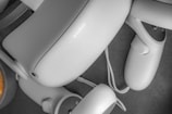 A close-up view of a virtual reality headset and controllers scattered on a surface. The equipment is sleek and modern, primarily gray in color, with smooth curves and a minimalist design.