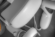 A close-up view of a virtual reality headset and controllers scattered on a surface. The equipment is sleek and modern, primarily gray in color, with smooth curves and a minimalist design.