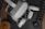 Various technology-related items are placed on a dark surface. A virtual reality headset with controllers is centrally located. Nearby, there is a black case, a tripod, and partially visible accessories including a wooden coaster or speaker.